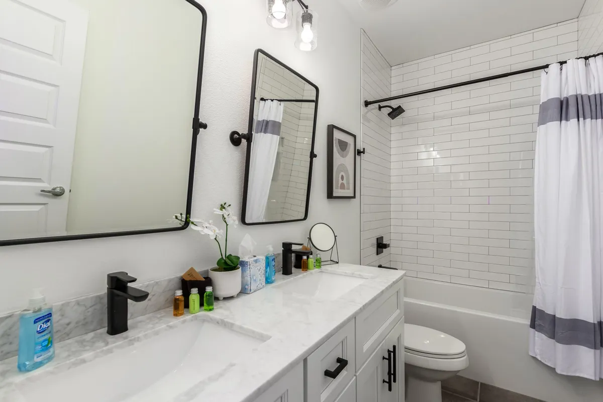 A modern bathroom featuring double vanity sinks, large mirrors, a spacious shower area, and tasteful decorative artwork. The finishes and layout evoke a serene, spa-like atmosphere.