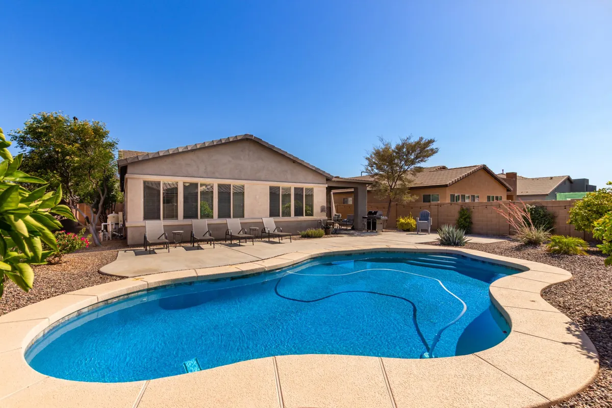 This exterior shot highlights a sparkling swimming pool surrounded by a well-designed patio and lush landscaping. The mood is leisurely and refreshing, with hints of social possibility—a perfect place for swimming, sunbathing, or gathering with friends for an evening barbecue.