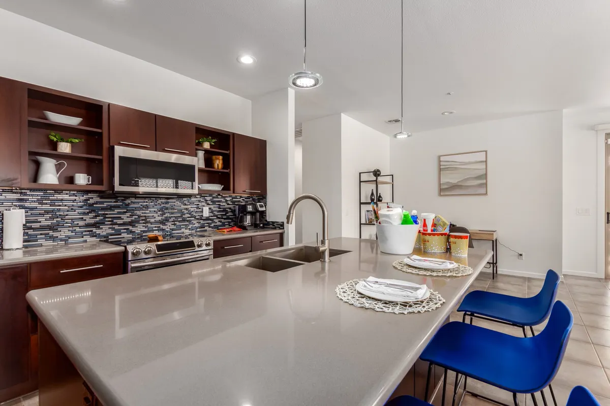 A stylish kitchen with a spacious island, stainless steel appliances, and blue chairs. The scene exudes warmth and readiness for both family meals and entertaining, with space for cooking and casual conversation at the breakfast bar.