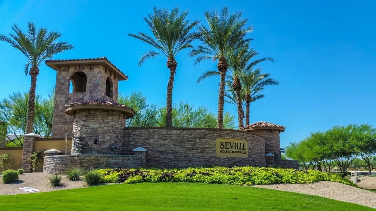This image captures the exterior of the Seville Country Club area, featuring a distinctive stone tower, palm trees, and clear signage that communicates the club's prestigious ambiance. The scene suggests activities such as golfing, social events, and outdoor gatherings, all set in a relaxed, inviting atmosphere with warm sunset lighting.