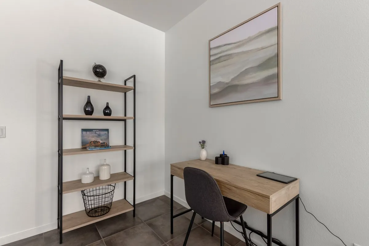 A serene workspace setup with a wooden desk, open shelving, and framed artwork, offering a dedicated area for remote work or long-term stays. The space is thoughtfully organized and visually appealing.
