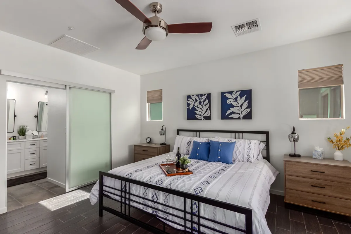 A stylish queen bedroom featuring a neatly made bed with decorative pillows, framed artwork on the wall, and nightstands with lamps and thoughtful decor. Soft lighting and cozy textiles create a welcoming and restful atmosphere.