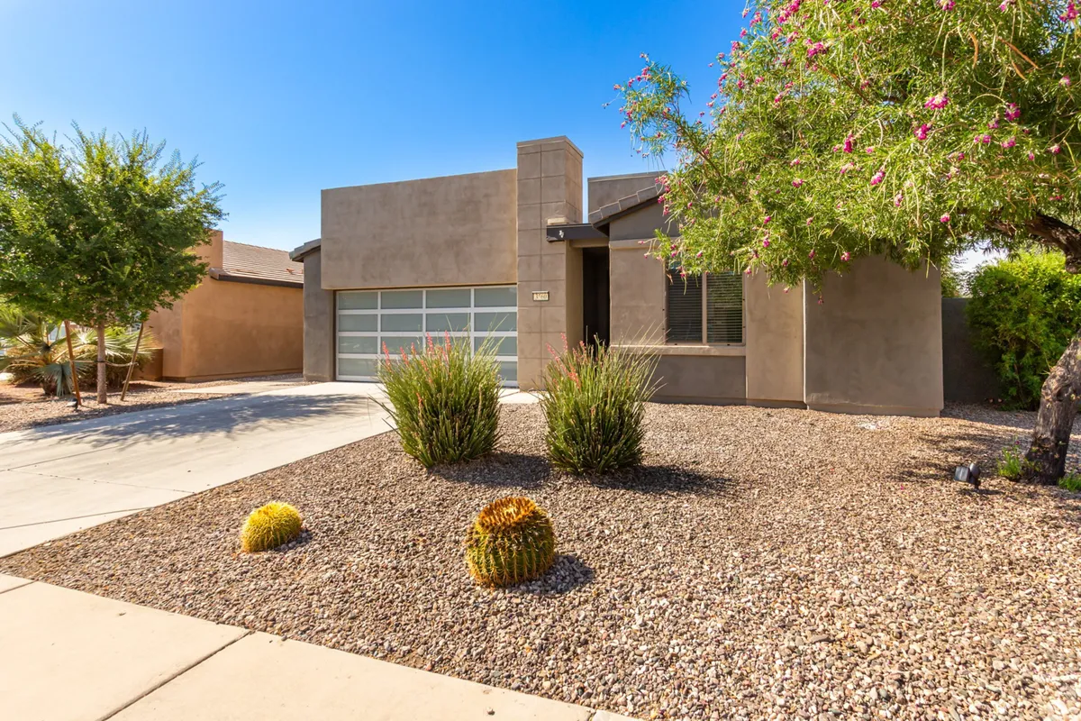 The home's striking modern architecture is showcased against a backdrop of carefully landscaped desert plants and cacti. The front yard is welcoming, with shaded areas suitable for relaxing with morning coffee or enjoying the sunset.